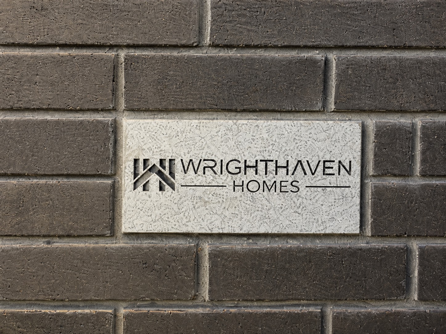 The WrightHaven Homes name cut into a stone marker set in a brick entrance wall.